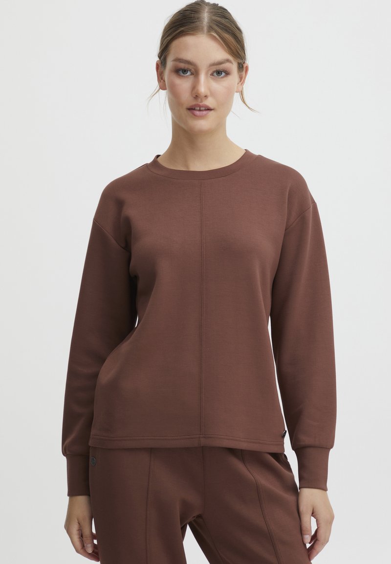 Felpa marrone con maniche lunghe, polsini a coste e collo tondo. Presenta un dettaglio di cucitura centrale e una texture liscia. Abbinata a pantaloni coordinati.