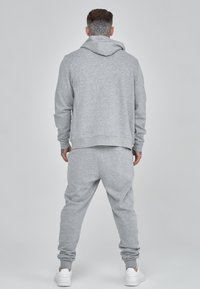 Sudadera gris y joggers a juego hechos de una tela suave. La sudadera tiene un cordón ajustable. El conjunto tiene puños y cintura acanalados.