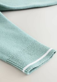 Helle blaue gestrickte Ärmelbündchen mit einem weißen Streifen nahe dem Rand, flach auf einer hellen Oberfläche liegend.