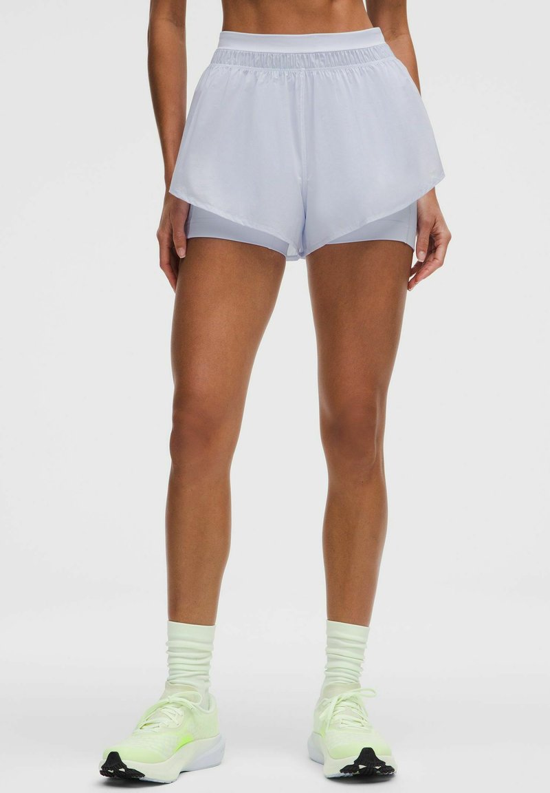 Pantalones cortos deportivos de color azul claro con un diseño en capas, que cuentan con una textura suave y lisa, y una cinturilla elástica, combinados con zapatillas de neón.