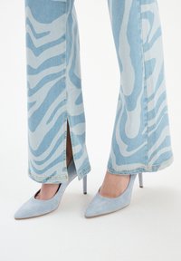 Jasnoniebieskie dżinsowe spodnie z szerokimi nogawkami w biały wzór zebry, z bocznymi rozcięciami. Połączone z jasnoniebieskimi zamszowymi butami na wysokim obcasie.