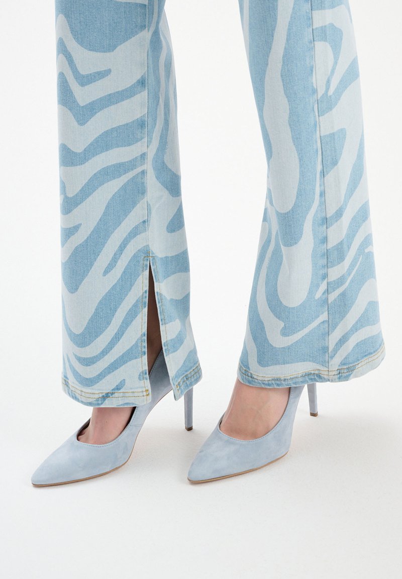 Jasnoniebieskie dżinsowe spodnie z szerokimi nogawkami w biały wzór zebry, z bocznymi rozcięciami. Połączone z jasnoniebieskimi zamszowymi butami na wysokim obcasie.