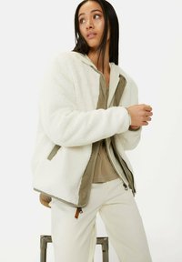 Cremfarbener Fleece-Jacke mit kontrastierendem olivgrünem Futter, Reißverschluss vorne und gerippten Bündchen. Der Stoff hat eine weiche, strukturierte Oberfläche.