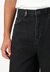 Svarte denimjeans har en avslappet passform, fem lommer og karakteristisk søm. Midjebåndet har en metallknapp og merket løkke-klistremerke.