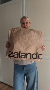 Busta di carta marrone con la scritta 'zalando' stampata in bold letters neri, tenuta davanti a una persona, con una texture accartocciata.