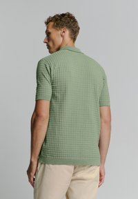 Korte mouwen polo shirt van textuurstof in lichtgroen, met een kraag en ribgebreide manchetten, gedragen met een lichtgekleurde broek.