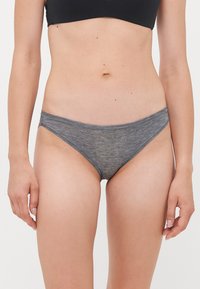 Woman wearing gray cotton bikini-style underwear and a black crop top, standing against a plain light background.