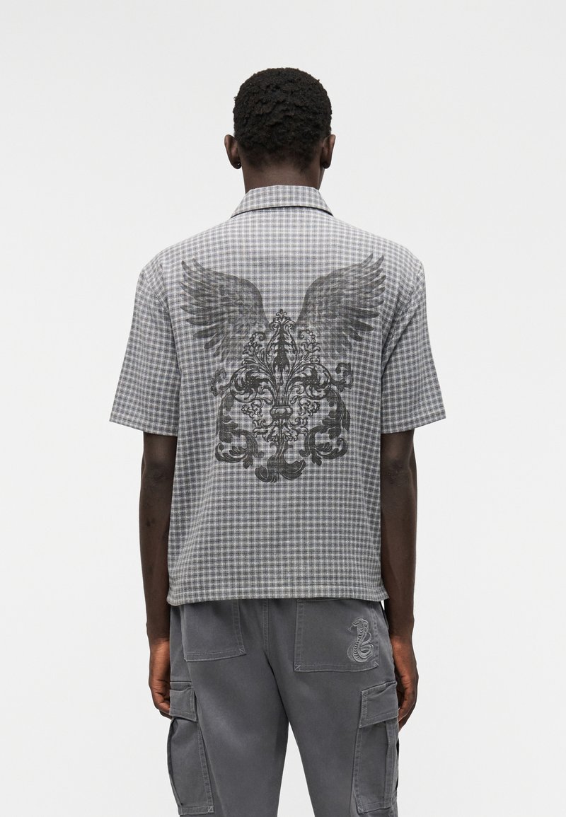 Πουκάμισο με κοντό μανίκι, καρό σε γκρι απόχρωση με φτερό και μπαρόκ σχέδιο μαύρο στο πίσω μέρος. Σχεδίαση με γιακά και άνετη εφαρμογή.