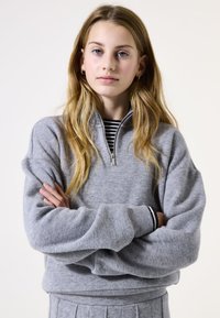 Grijze fleece pullover met een half-rits kraag, geribde manchetten en een luxe textuur. Draagt over een zwart-wit gestreept shirt.