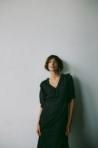 Crna haljina s kratkim napuhanim rukavima, teksturirane tkanine, v-izrezom i naglašavanjima od čipke. Dizajn uključuje uski struk i lepršavu suknju.