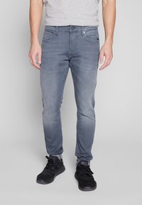 Bleka gråjeans med slim fit, medelhög midja, subtila slitna detaljer och femficksdesign, i kombination med svarta sportskor.