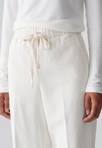 Pantalons de loungewear blancs à rayures, dotés d'une taille à cordon et d'une texture douce, associés à un haut ajusté à manches longues blanc.