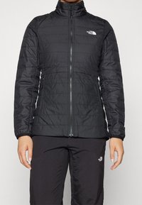 Svart puffjacka med hög krage, dragkedjestängning, horisontell sömnad och logotypdetalj på vänster bröst. Slätt, lättviktigt tyg.