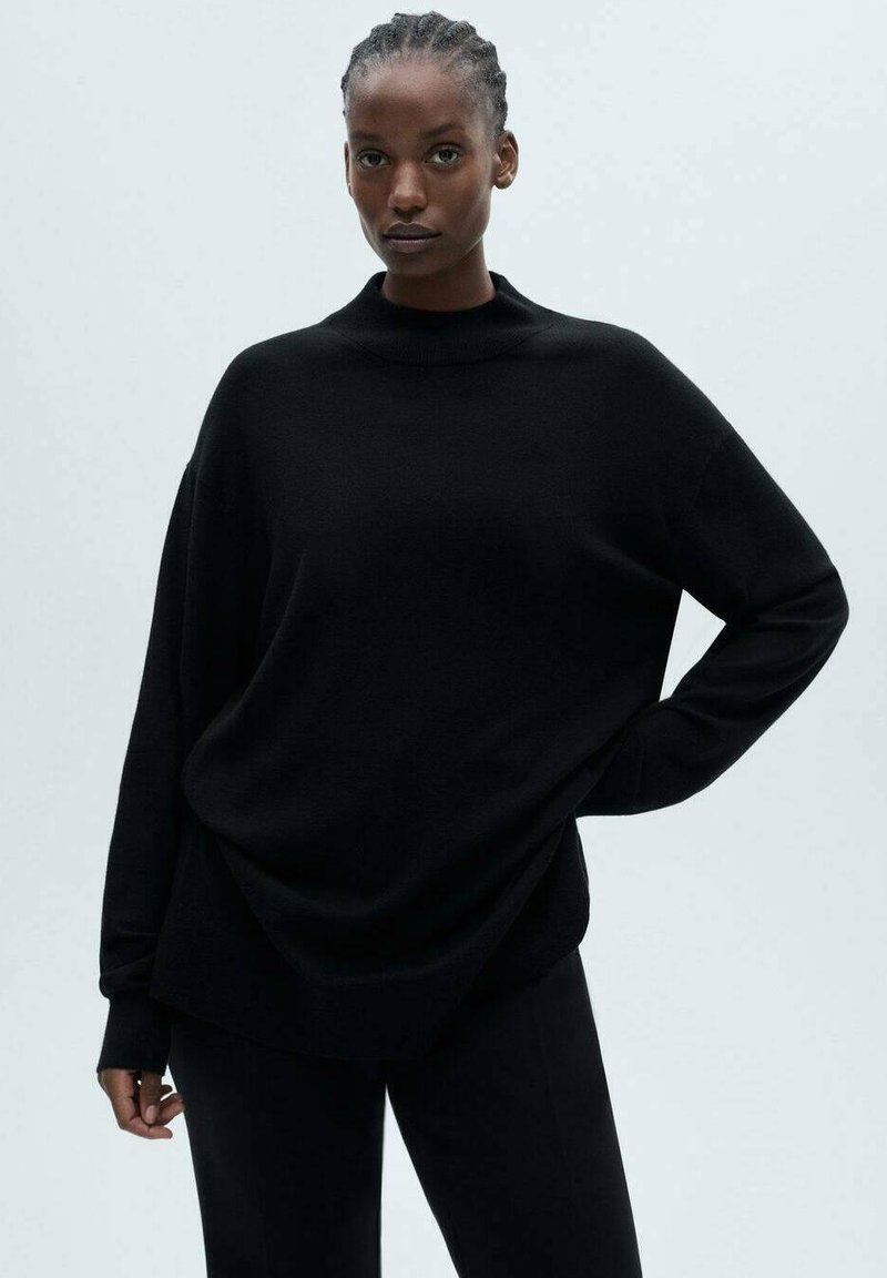 Crni pletena džemper sa visokim izrezom, spuštenim ramenima i opuštenim krojem. Glatka tekstura, u kombinaciji sa odgovarajućim crnim hlačama.