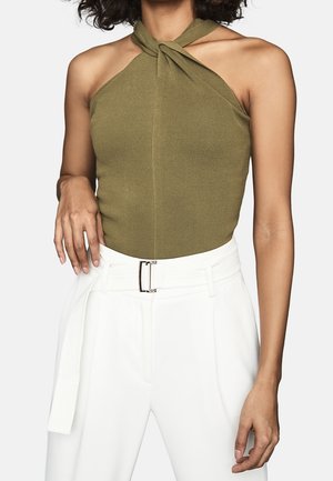 Zielony oliwkowy top na szyję z wiązanym dekoltem, o prążkowanej fakturze, w połączeniu z białymi spodniami z wysokim stanem i paskiem z srebrną klamrą.