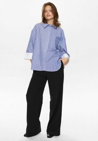Blue and white striped shirt with a relaxed fit, button-down front, and rolled-up white cuffs, paired with black wide-leg pants.