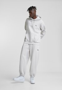 Lys grå hoodie og matchende sweatpants lavet af blødt stof. Har en frontlomme og elastiske manchetter. Hvide sneakers fuldender outfittet.