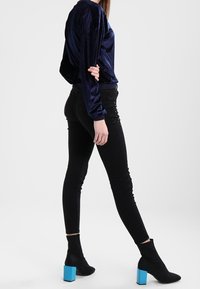 Top a maniche lunghe in velluto blu navy abbinato a pantaloni skinny neri con dettagli in borchie e stivali neri con tacco blocco blu.