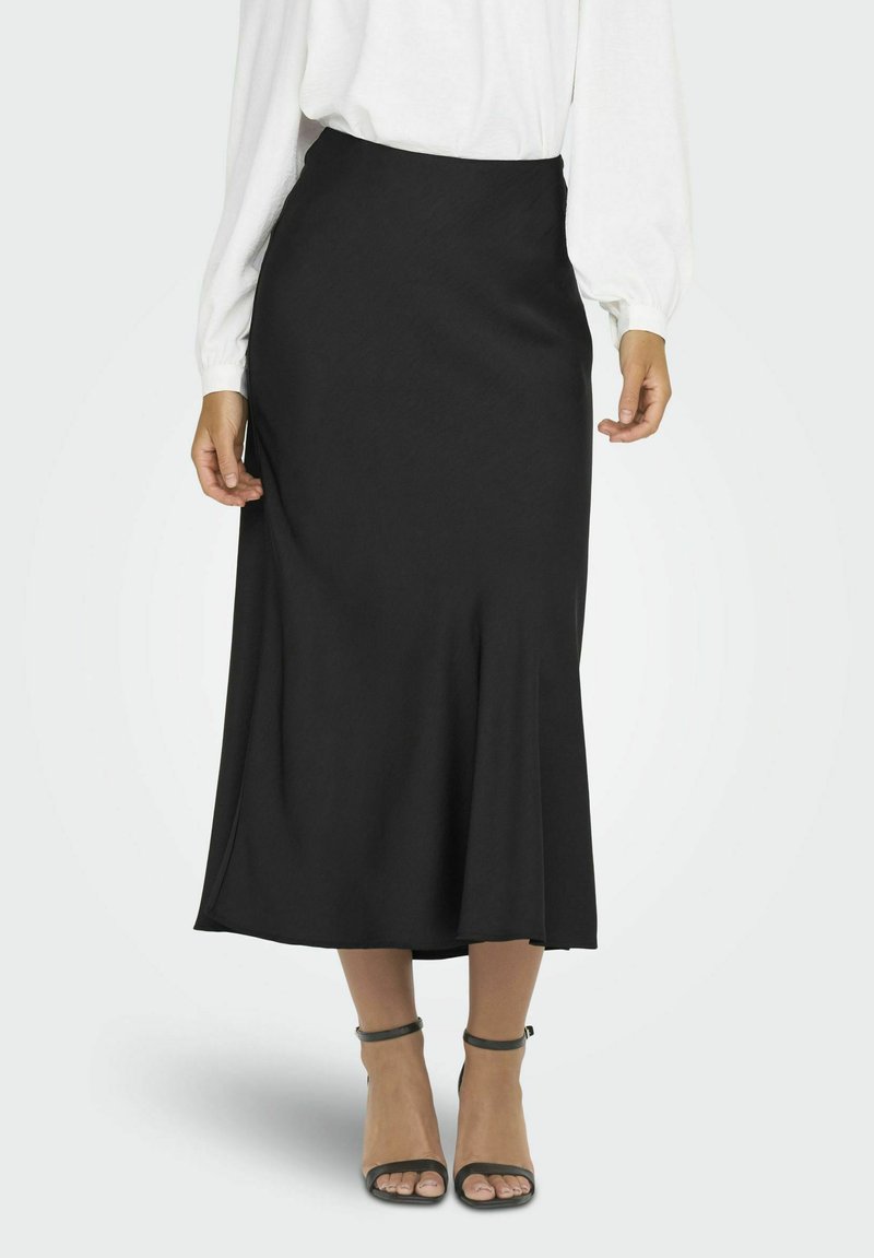Jupe midi noire avec un ourlet évasé, confectionnée en tissu lisse. Portée avec une blouse blanche et associée à des escarpins à bride cheville gris.