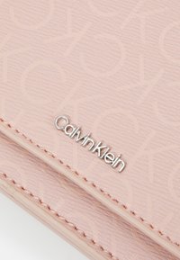 Calvin Klein pung i struktureret lyserødt materiale med præget logo mønster og sølvfarvet branding.