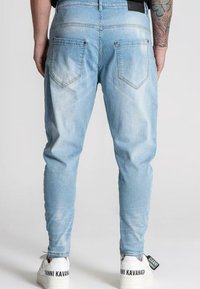Ljusblå denimjeans med tapered passform, fem fickor, blekningsdetaljer och en svart varumärkesetikett i midjan bak. Bärs med vita sneakers.