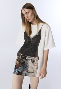 T-shirt with a graphic print depicting a black camisole and denim shorts, featuring a loose fit, short sleeves, and a light background.