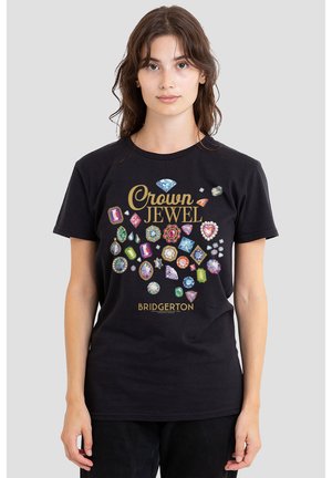 Junge Frau trägt ein schwarzes Bridgerton-T-Shirt mit bunten Edelstein-Illustrationen und dem Text "Crown Jewel" in goldener Schrift.