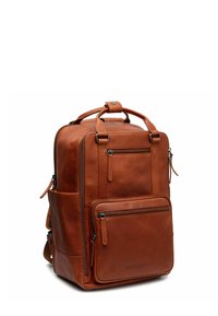 Sac à dos en cuir marron avec plusieurs compartiments zippés, poignées robustes et bretelles réglables. Présente une texture lisse et un design minimaliste.