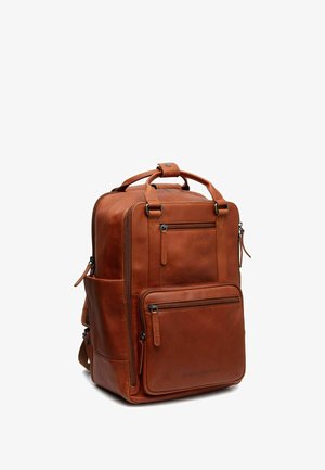 Sac à dos en cuir marron avec plusieurs compartiments zippés, poignées robustes et bretelles réglables. Présente une texture lisse et un design minimaliste.