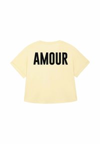 Dzeltena t-kreklu ar vārdu "AMOUR" biezās melnās burtos uz muguras. Vienkāršs, ikdienišķs dizains ar īsām piedurknēm.