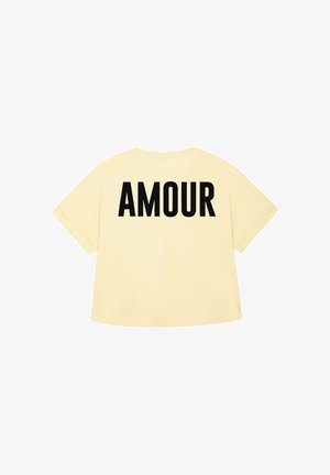 Geel T-shirt met het woord "AMOUR" in vette zwarte letters op de achterkant. Eenvoudig, casual ontwerp met korte mouwen.