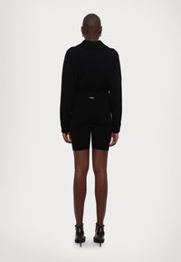 Maglione nero lavorato a maglia con colletto alto, abbinato a pantaloni corti da bicicletta neri. Il look è completato da scarpe a strappo nere con tacco alto.