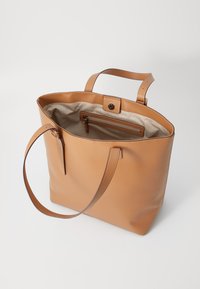 Bruine leren totebag met een open bovenkant, twee lange handvatten en een gestreepte stoffen voering. Beschikt over een interne ritszak voor opslag.