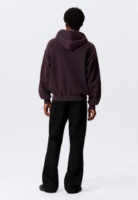 Sweatshirt met capuchon in donker bordeauxrood met een ontspannen pasvorm, geribbelde manchetten en tailleband. Gecombineerd met zwarte broek met wijde pijpen.