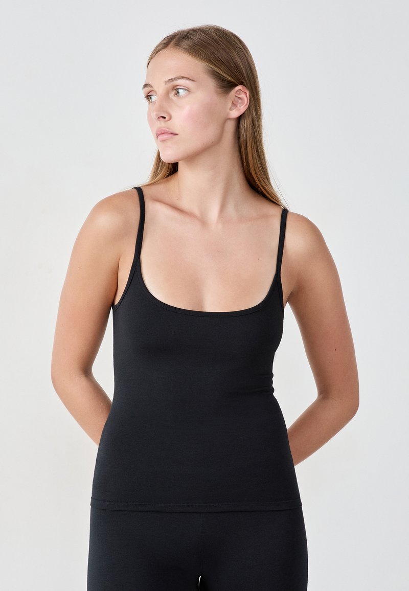 Débardeur noir à fines bretelles et encolure arrondie. Fabriqué en tissu doux et extensible avec une silhouette ajustée. Texture lisse.