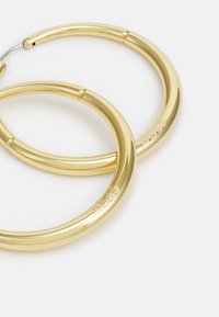 Pendientes de aro de oro con un diseño suave y redondeado. Presentan un cierre de bisagra y una marca grabada. Superficie reflectante con un acabado pulido.