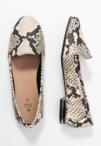 Une paire de chaussures plates avec un motif en peau de serpent noir et blanc, l'une vue de dessus et l'autre de côté.