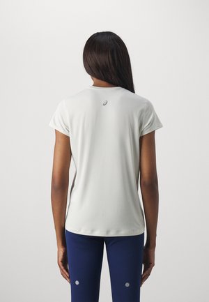 Kvinde med langt mørkt hår, stående med ryggen mod kameraet, iført en lysegrå kortærmet skjorte og marineblå leggings.