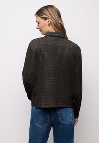 Camicia a quadri marrone con bottoni, colletto e maniche lunghe, realizzata in tessuto strutturato, abbinata a jeans di denim blu.