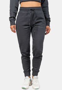 Graue Jogginghosen mit einem Kordelzugbund, gerippten Bündchen und einem dezenten Logodetail an der Seite, kombiniert mit weißen Turnschuhen.