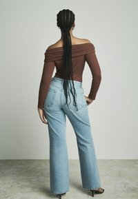 Haut marron à épaules dénudées avec des manches longues, associé à un jean large en denim clair taille haute. Cheveux tressés tombant dans le dos.
