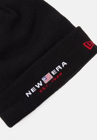 Berretto nero di maglia con logo ricamato "NEW ERA" in bianco, una piccola bandiera americana e "EST. 1920" in rosso. Tessuto morbido, design con risvolto.