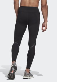 Black athletic leggings featuring a high waistband, slim fit, and reflective accents. Paired with gray running shoes.