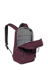 Zaino color marrone con schiena e spallacci imbottiti, interno grigio, compartimenti con zip e una toppa del logo sul davanti. Tessuto di texture liscia.
