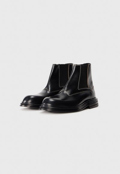 Bottines Chelsea en cuir noir avec des panneaux latéraux élastiques, des bouts ronds, des surpiqûres contrastées et une semelle épaisse et texturée.