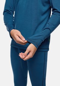 Blaues Langarm-Sportoberteil mit lockerer Passform, flachen Nähten und Daumenlöchern, kombiniert mit passenden Leggings mit glatter Textur.