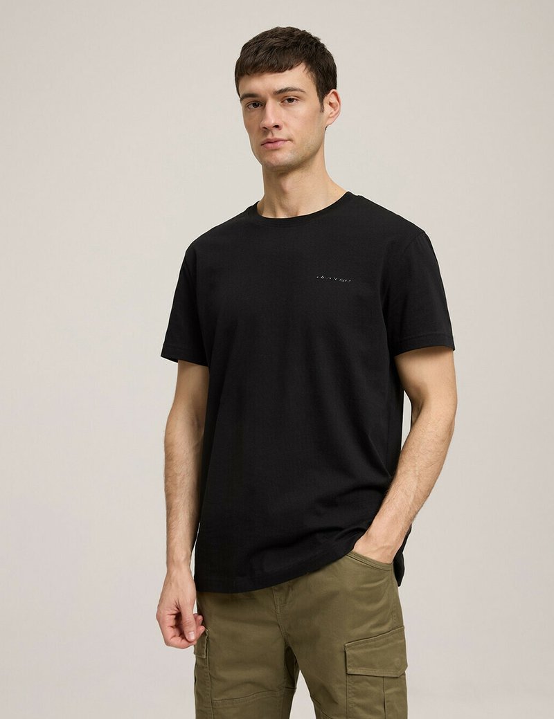 Czarny bawełniany t-shirt z okrągłym dekoltem i małym graficznym detalem na piersi, zestawiony z oliwkowymi spodniami cargo.