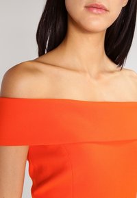 Schulterfreies Kleid aus glattem, leuchtend orangefarbenem Stoff, mit einem strukturierten Ausschnitt und einer enganliegenden Silhouette.
