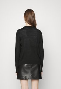 Pull en tricot noir à manches longues, avec un col arrondi et un ourlet côtelé, associé à une mini-jupe en cuir noire.
