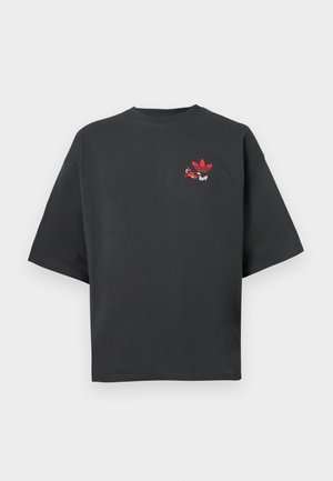 Μαύρο υπερμεγέθες T-shirt με μικρό κόκκινο λογότυπο Adidas και καρτούν χαρακτήρα στο αριστερό στήθος, με φόντο απλό ανοιχτό γκρι.